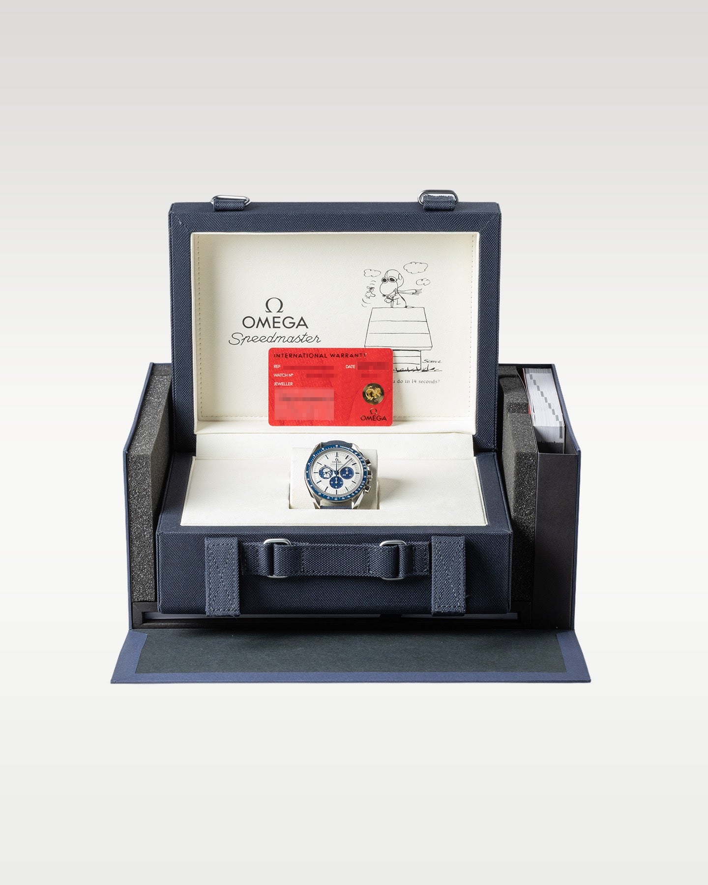 The complete luxury collector presentation layout showing the 2022 Snoopy Speedmaster watch resting inside its oversized blue woven fabric travel case and inner storage chest
