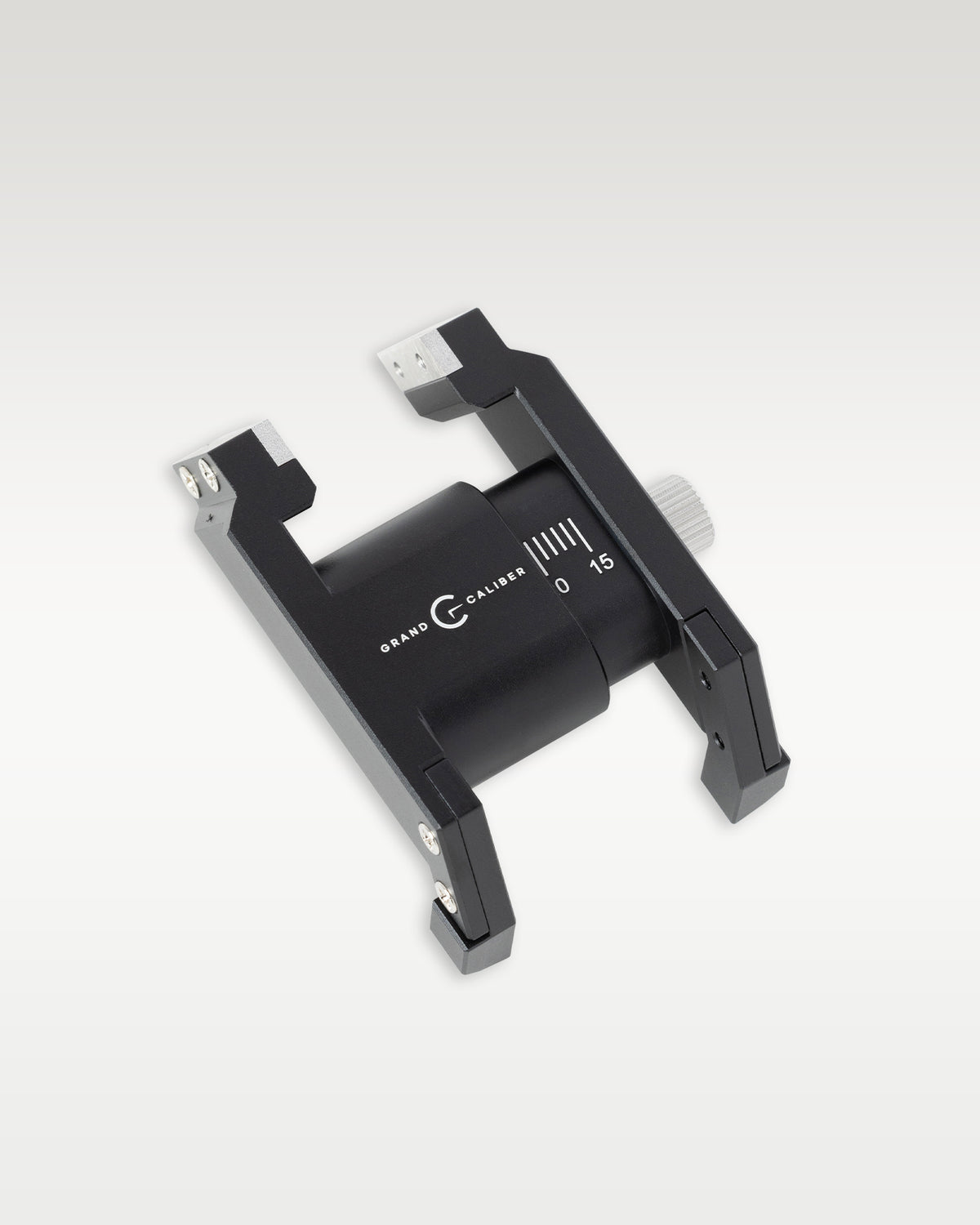 Angled view of a black anodized Grand Caliber precision watch case holder tool with millimeter measurement markings and silver adjustment knob
