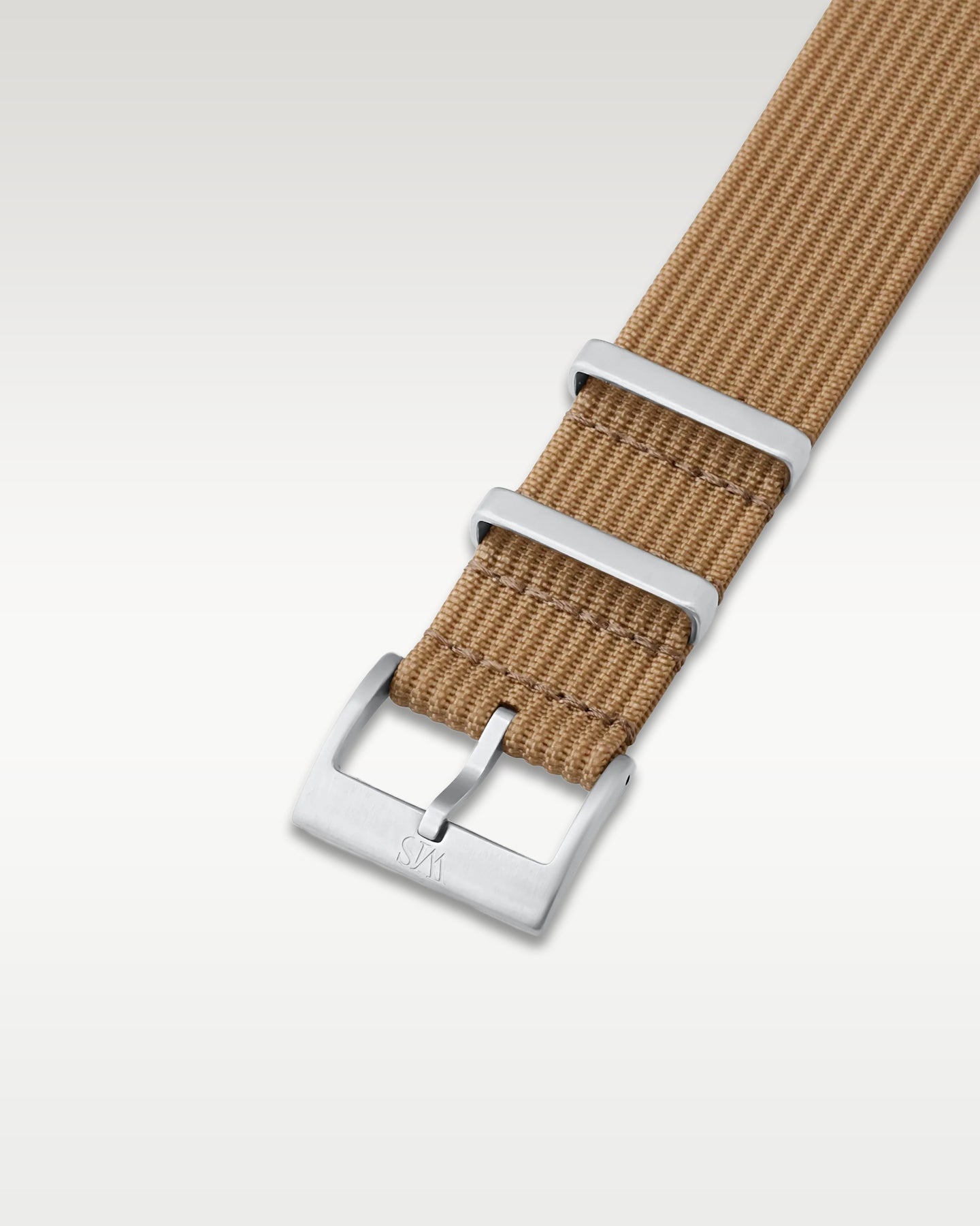 Angled detail shot of a sandy desert tan nylon watch band showing its pre-installed brushed silver pin buckle
