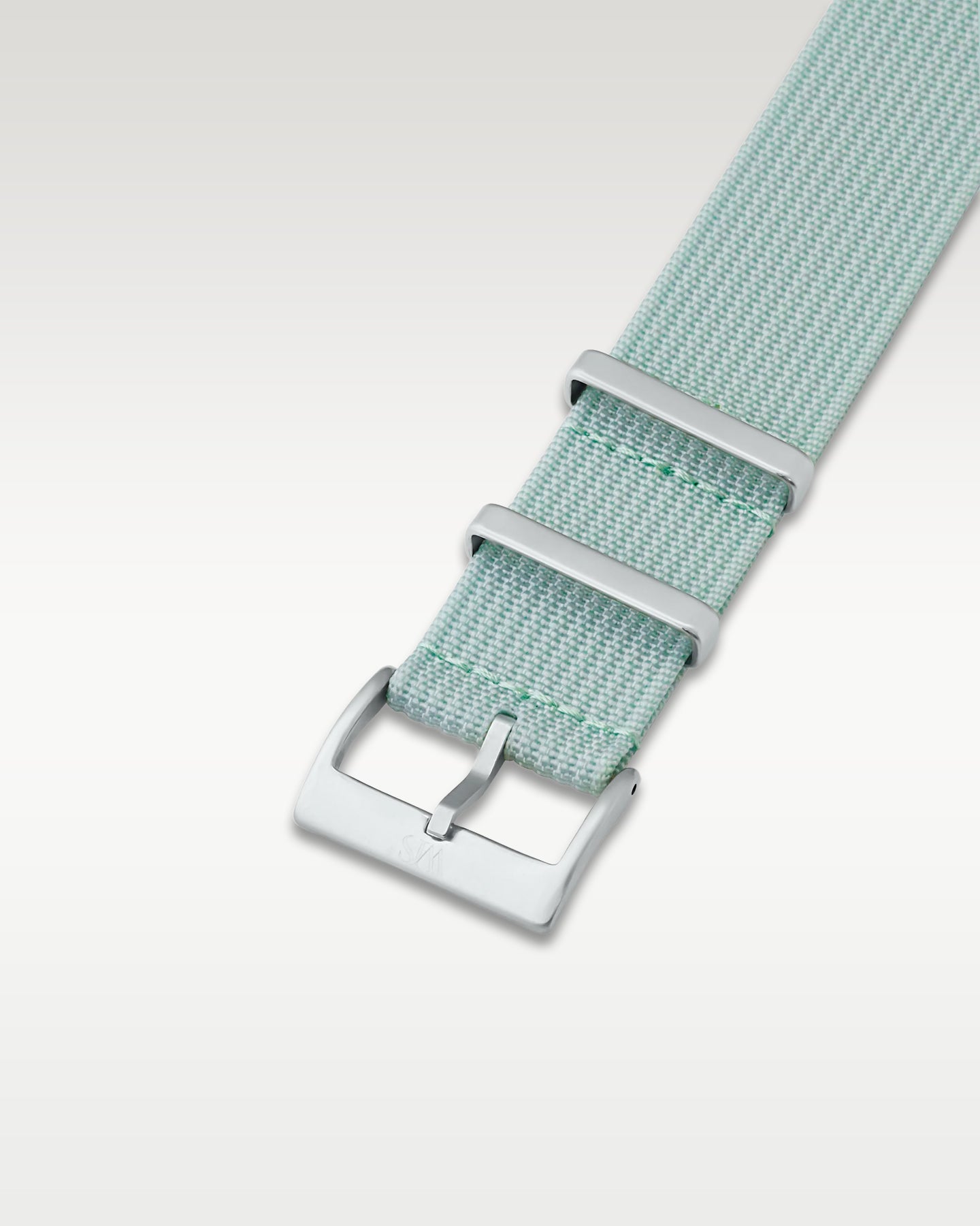 Angled detail shot of a subtle sage green nylon watch band showing its pre-installed brushed silver pin buckle