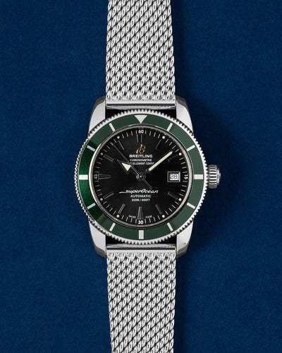 Pre-owned Breitling Superocean Heritage 42 A17321 stainless steel watch with black dial and green bezel on a mesh bracelet at Grand Caliber Dallas
