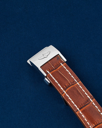 An angled portrait of the premium honey-brown cognac alligator skin strap with white contrast stitching, secured by a polished stainless steel folding safety clasp