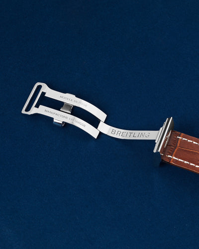 Close up flat lay view of the inner mechanical folding linkage arms of the open stainless steel Breitling deployment clasp mechanism against a navy blue backdrop