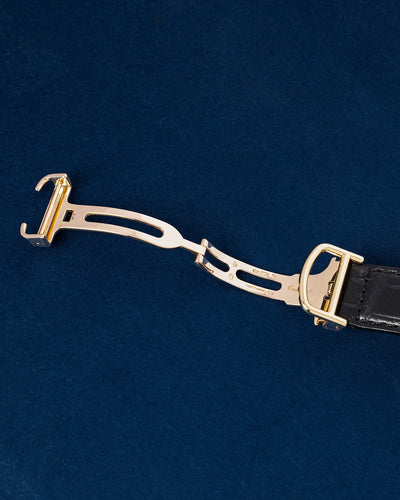 Close-up studio view of the open solid gold multi-blade folding deployant clasp on a black alligator leather Cartier watch strap