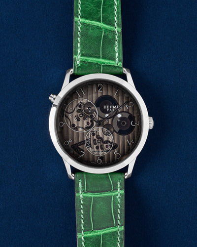 2024 Hermès Slim d'Hermès Squelette Minuit W054192WW00 platinum skeleton watch with a vibrant green alligator strap on a blue background