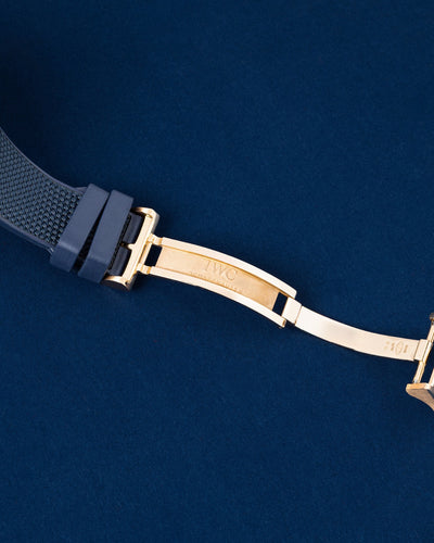 Close-up studio view of the open solid gold multi-blade folding deployment clasp on an IWC blue rubber strap