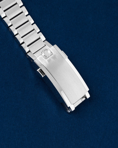 Close-up view of the closed vintage-style flat-link stainless steel bracelet featuring the engraved Omega logo on the comfort-adjust clasp