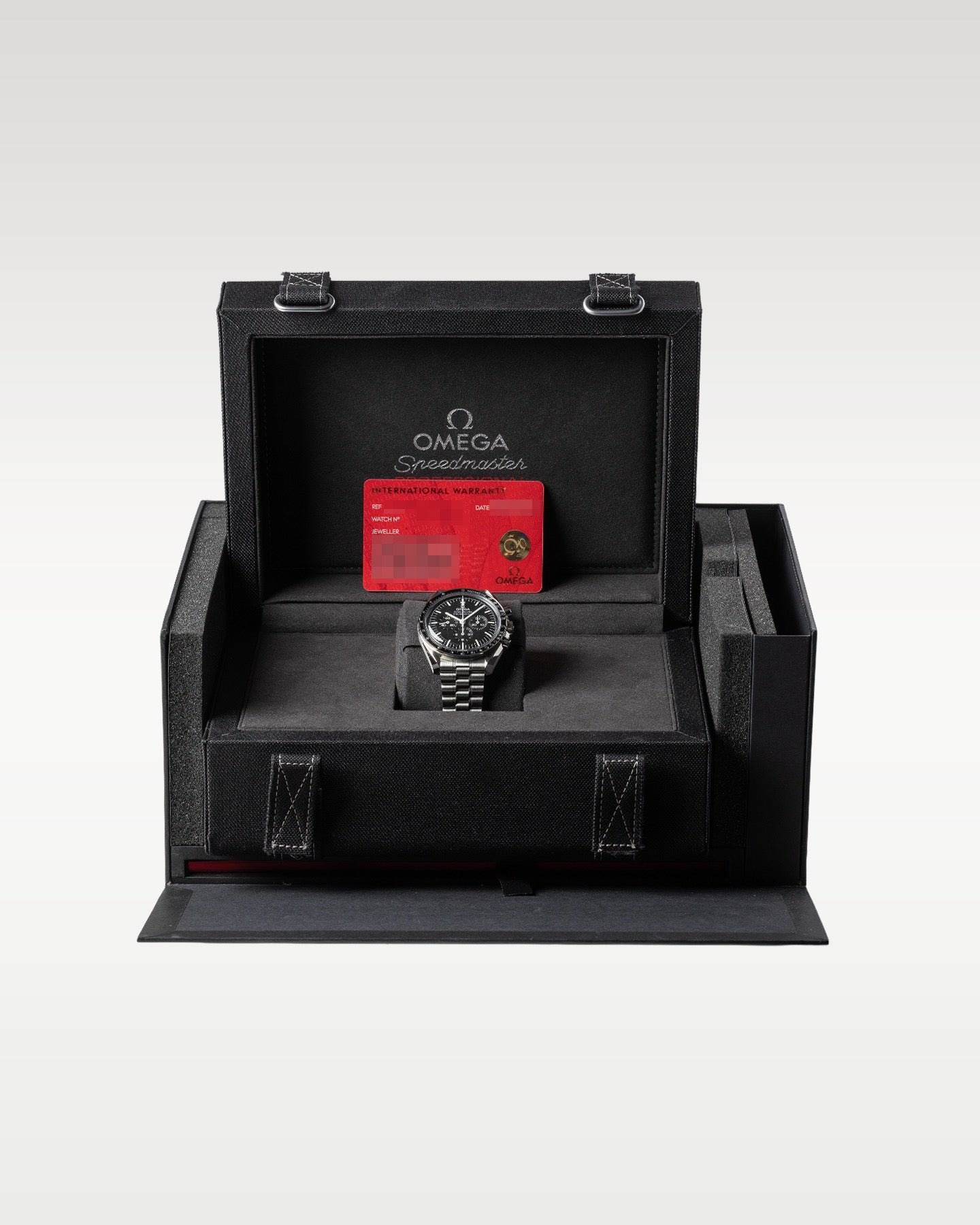 An open oversized black luxury Speedmaster Moonwatch flight box displaying the chronograph watch and red warranty cards nested inside