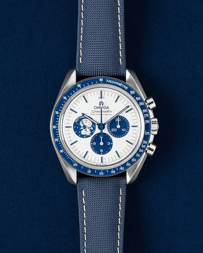 A pre-owned 2022 Omega Speedmaster Silver Snoopy Award 50th Anniversary chronograph showcasing its Ag925 silver dial, blue subdials, and matching blue nylon fabric strap at Grand Caliber in Dallas
