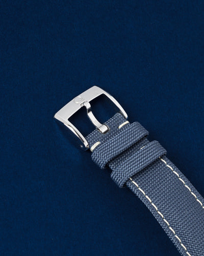 Close-up view of the blue structured fabric strap showing its contrasting white stitching and the official satin-brushed stainless steel tang buckle clasp