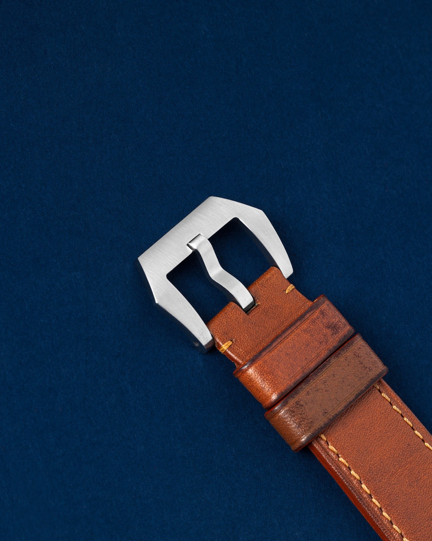 An angled  photograph of the tan leather strap focusing on the secure closure of the brushed stainless steel tang buckle for the Panerai Luminor Marina Logo PAM 00005 at Grand Caliber in Dallas, Texas