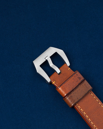 An angled  photograph of the tan leather strap focusing on the secure closure of the brushed stainless steel tang buckle for the Panerai Luminor Marina Logo PAM 00005 at Grand Caliber in Dallas, Texas