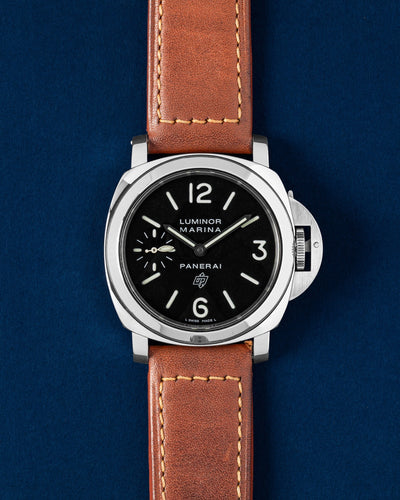 A preowned 2005 Panerai Luminor Marina Logo PAM 00005 displaying its original black dial luminescent hands and signature oversized crown guard mechanism with a brown leather strap at Grand Caliber in Dallas, Texas
