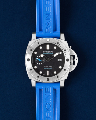 A preowned 2022 Panerai Submersible PAM01229 displaying its original black dial with high contrast markers robust steel case and striking blue rubber strap at Grand Caliber in Dallas, Texas