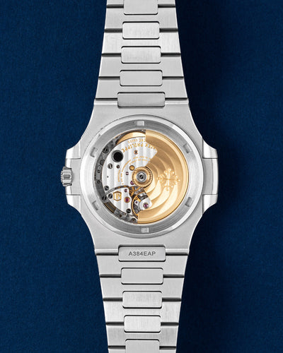 Rear exhibition profile through a sapphire crystal revealing the self winding mechanical movement of the Patek Philippe Nautilus 5711 with its solid gold rotor against a dark blue surface at Grand Caliber in Dallas, Texas