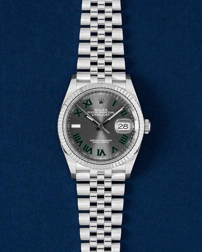 frontal studio portrait of the 36mm Rolex Datejust 126234 Wimbledon watch featuring a slate dial with green-bordered Roman numerals and a Jubilee bracelet resting on a navy blue background