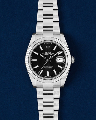 frontal studio portrait of a White Rolesor Rolex Datejust 41 126334 featuring a black sunray dial, fluted white gold bezel and Oyster bracelet resting on a navy blue background