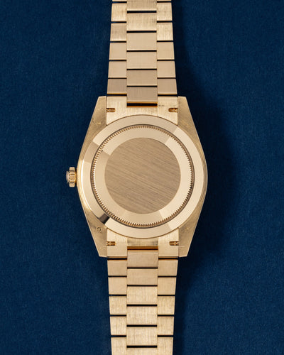The reverse orientation of the 40mm yellow gold watch head showcasing its solid fluted Oyster caseback and polished tapering lugs against a navy blue backdrop