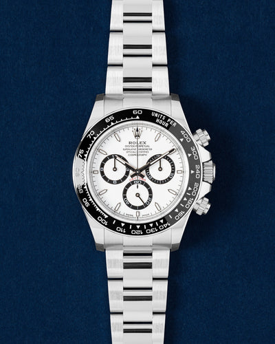 Brand new 2026 Rolex Cosmograph Daytona 126500LN Panda watch featuring a white dial, black ceramic tachymeter bezel and steel Oyster bracelet on a navy blue studio background