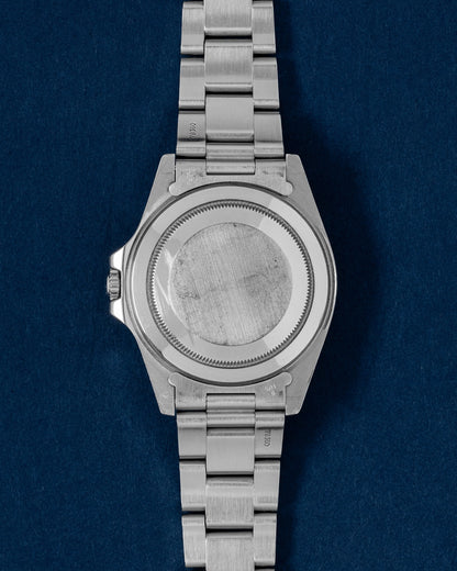 The reverse orientation of the 40mm oystersteel sports chassis highlighting its original period-correct flat-brushed solid screw-down caseback against a dark navy blue background