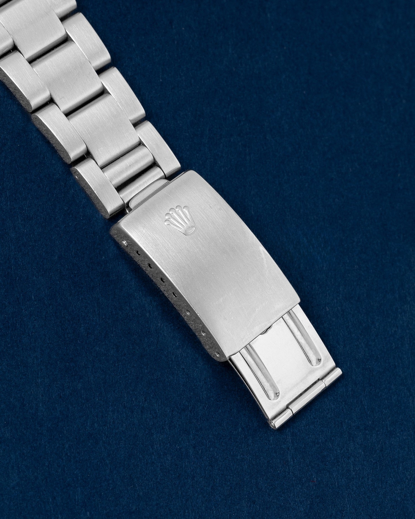 An angled portrait of the satin-finished three-piece link Oyster bracelet focusing on the secure closure of the vintage period-correct stamped single-lock folding buckle detailed with the Rolex crown emblem