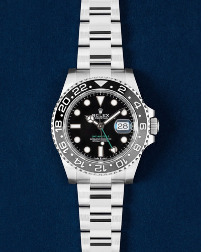2025 Rolex GMT-Master II 126710GRNR Bruce Wayne watch featuring a black and grey ceramic bezel on a navy blue studio background