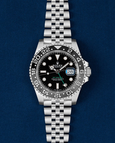 40mm Rolex GMT-Master II 126710GRNR Bruce Wayne watch featuring a black and grey ceramic bezel and Jubilee bracelet resting on a navy blue background