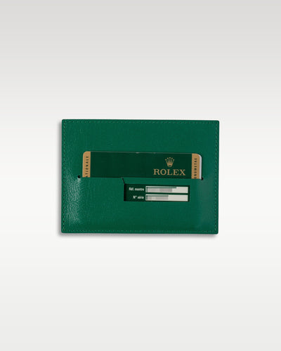 A top down view of the traditional green textured leather vertical document wallet holding the original 2014 international registration guarantee card