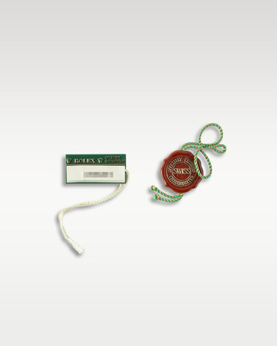 Official vintage red Rolex chronometer seal string tag alongside a green Swimpruf rectangular retail hang tag