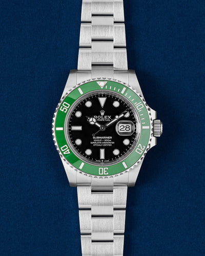 studio portrait of the 41mm Rolex Submariner Date 126610LV Starbucks watch featuring a green ceramic Cerachrom bezel and gloss black dial resting on a navy blue background
