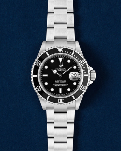 direct overhead frontal studio portrait of the 40mm stainless steel Rolex Submariner Date 16610 featuring a gloss black dial and black aluminum bezel on a blue background