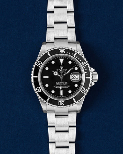 frontal studio portrait of a 2007 Rolex Submariner Date 16610 watch with a black dial and aluminum bezel insert resting on a navy blue background
