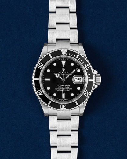 frontal studio portrait of a 2007 Rolex Submariner Date 16610 watch with a black dial and aluminum bezel insert resting on a navy blue background