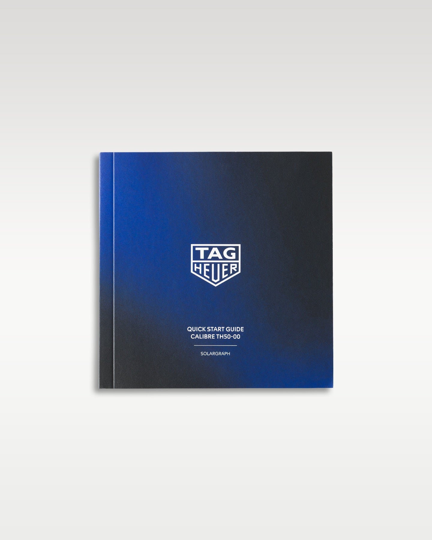 front cover of the black and blue gradient TAG Heuer user manual and technical operating instructions booklet displayed flat on a white studio backdrop