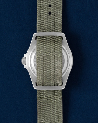 The solid titanium caseback of a Tudor Pelagos FXD GMT showing the integrated fixed strap bars and pass-through green fabric strap