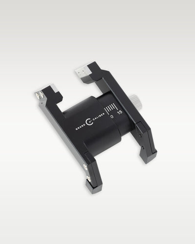 Angled view of a black anodized Grand Caliber precision watch case holder tool with millimeter measurement markings and silver adjustment knob