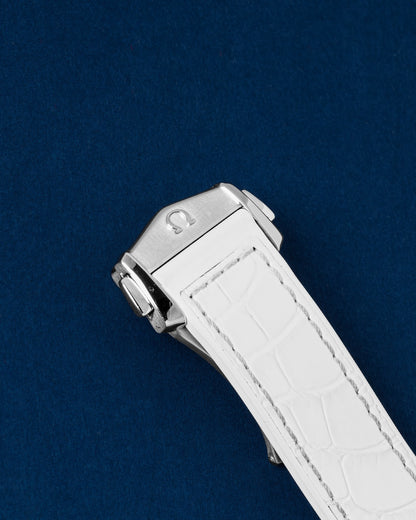 Close-up view of the closed stainless steel folding deployment clasp on an official white alligator grain rubber-lined Omega strap