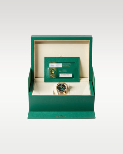 18k yellow gold Rolex Day-Date watch upright inside its open green presentation box alongside its warranty card holder