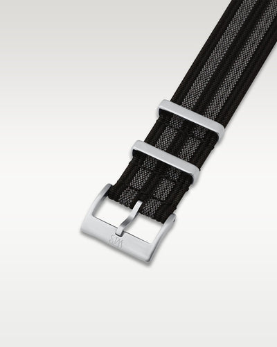 Angled detail shot of a black and grey bond-style nylon watch band showing the pre-installed brushed silver pin buckle