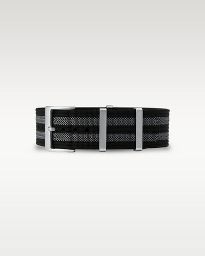 Flat view of a black and grey striped woven nylon watch strap folded with brushed steel keepers