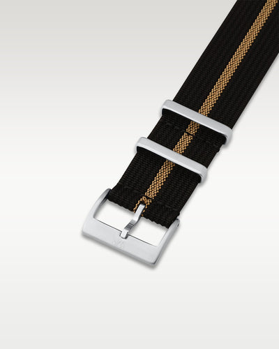 Angled detail shot of a black and khaki striped nylon watch band showing its pre-installed brushed silver pin buckle