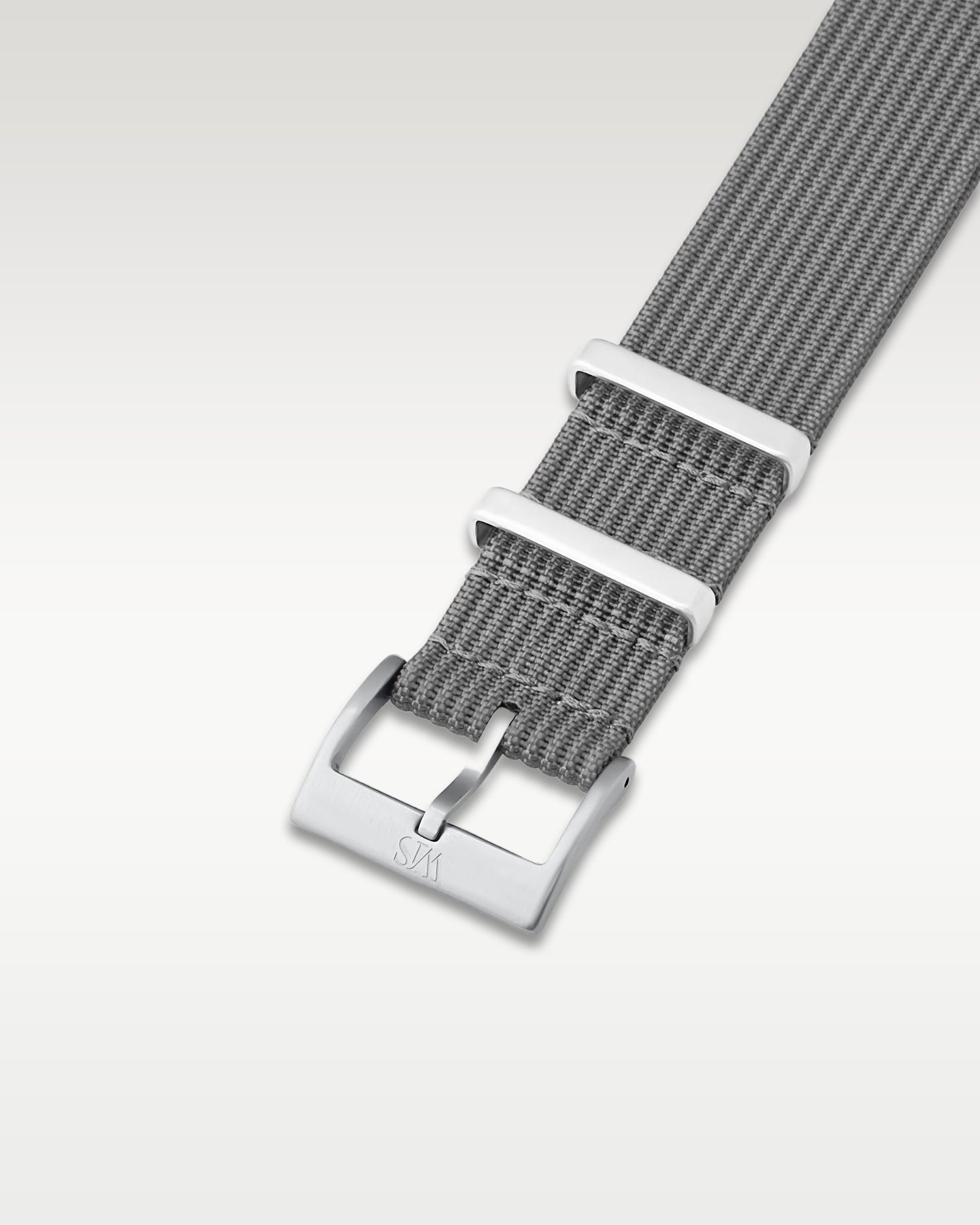 Angled detail shot of a charcoal grey nylon watch band showing its pre-installed brushed silver pin buckle