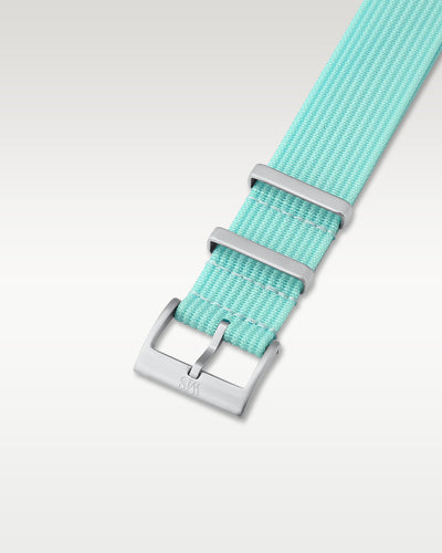 Angled detail shot of a lagoon blue nylon watch band showing its pre-installed brushed silver pin buckle