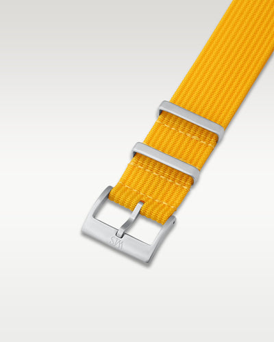 Angled detail view of a vibrant lemon yellow nylon watch band showcasing its brushed silver pin buckle