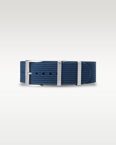 Flat layout view of a deep marine blue woven nylon watch strap folded with brushed silver hardware
