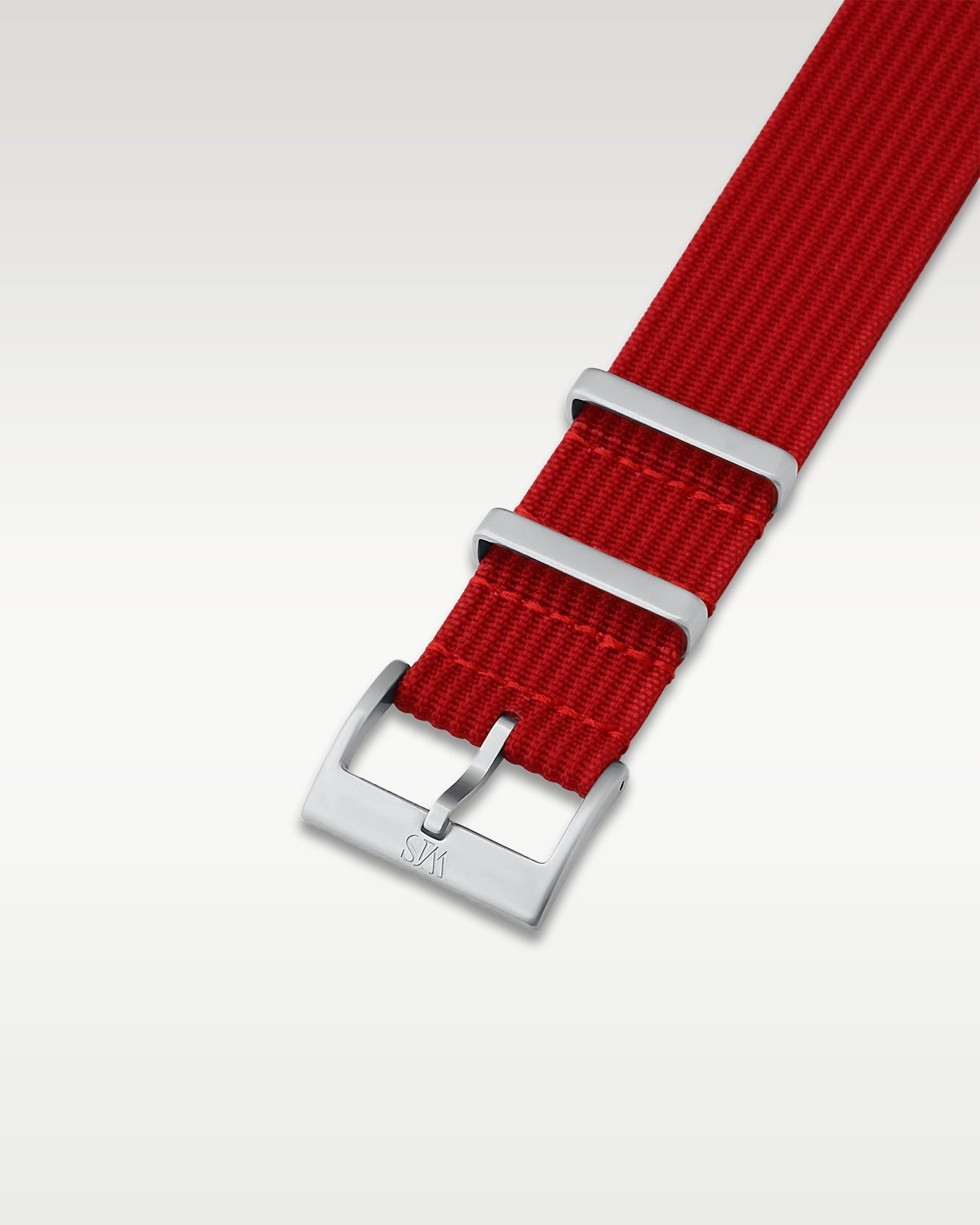 Angled detail shot of a deep scarlet red nylon watch band showcasing its brushed silver pin buckle