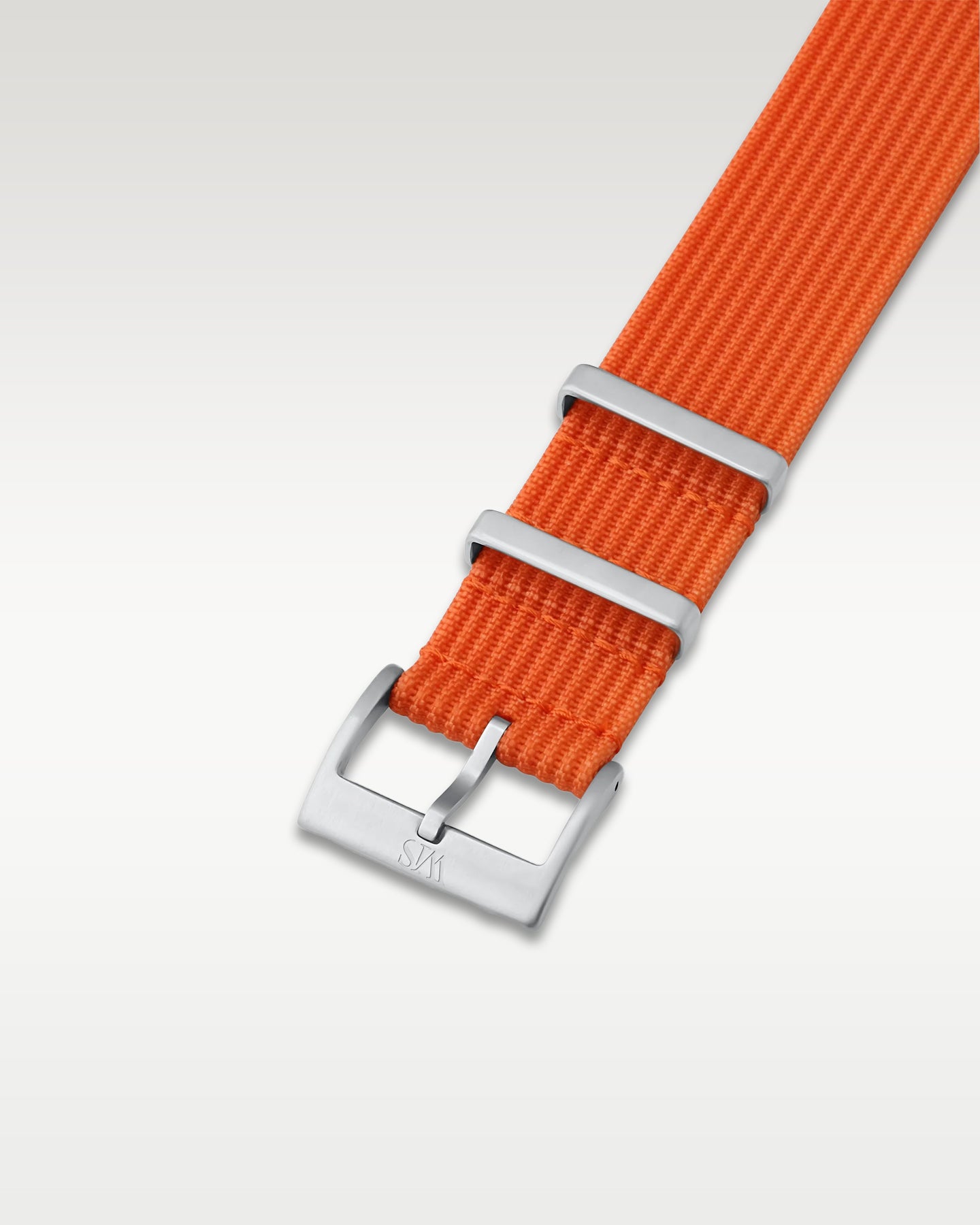 Angled detail shot of a bold tangerine orange nylon watch band showing its pre-installed brushed silver pin buckle