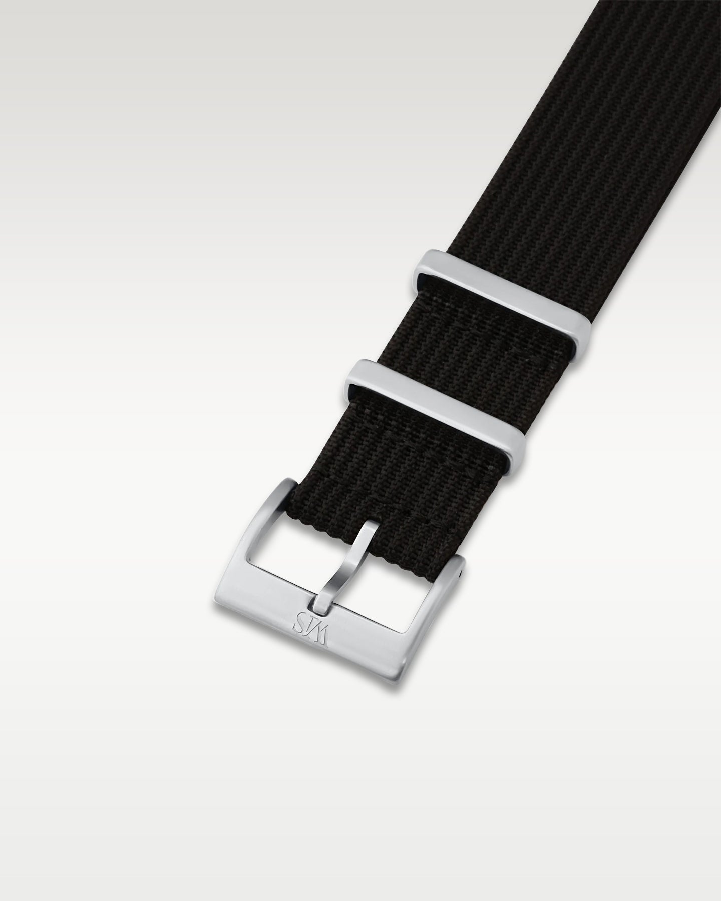 Angled detail view of a tuxedo black pull-through nylon watch band showcasing its pre-installed brushed silver pin buckle