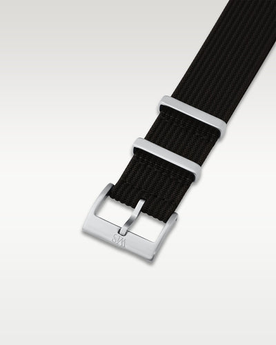 Angled detail view of a tuxedo black pull-through nylon watch band showcasing its pre-installed brushed silver pin buckle